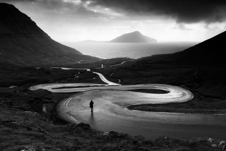 A person stands on a windy road in the Faroe Islands